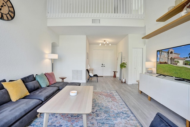 living room featuring an inviting chandelier, light wood-type flooring, visible vents, and a towering ceiling