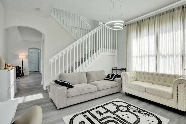 living area with baseboards, an inviting chandelier, stairs, wood finished floors, and arched walkways