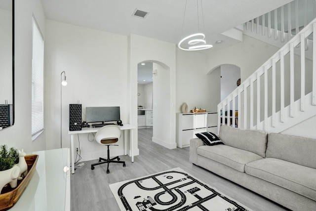 living room featuring a notable chandelier, stairway, visible vents, arched walkways, and light wood-style floors