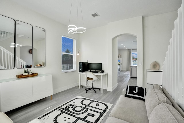 office with light wood finished floors, an inviting chandelier, visible vents, baseboards, and arched walkways
