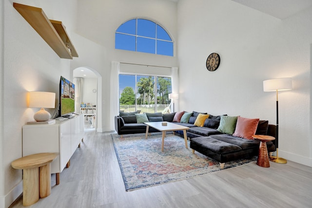 living area with a high ceiling, arched walkways, baseboards, and wood finished floors