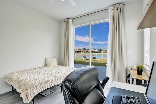 bedroom featuring a ceiling fan, a water view, wood finished floors, and access to exterior