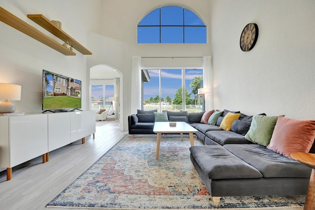 living area with a towering ceiling, a wealth of natural light, arched walkways, and wood finished floors
