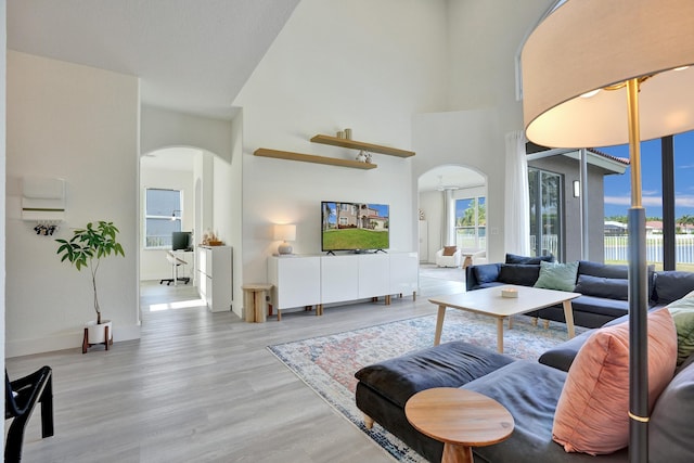 living room featuring arched walkways, light wood-style flooring, and a high ceiling