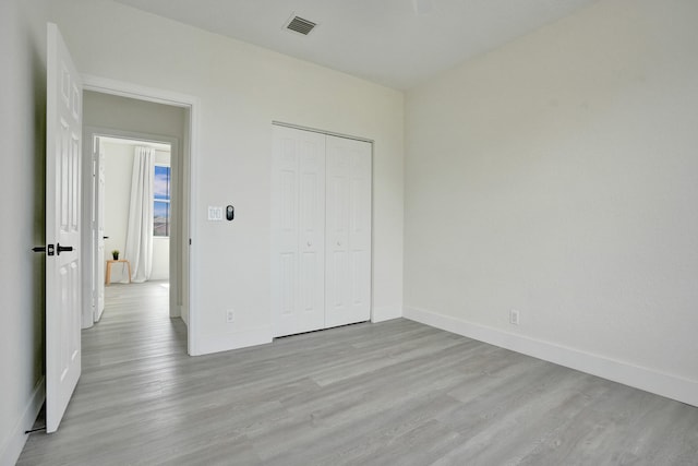 unfurnished bedroom featuring a closet, light wood-style floors, visible vents, and baseboards