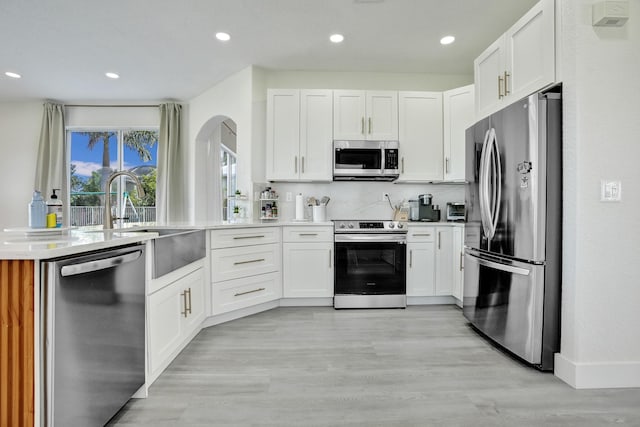 kitchen with light wood finished floors, white cabinetry, arched walkways, light countertops, and appliances with stainless steel finishes