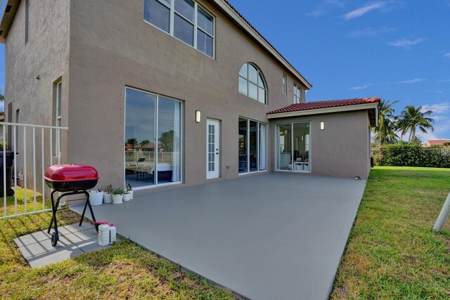 rear view of house featuring a lawn, a tiled roof, fence, a patio area, and stucco siding