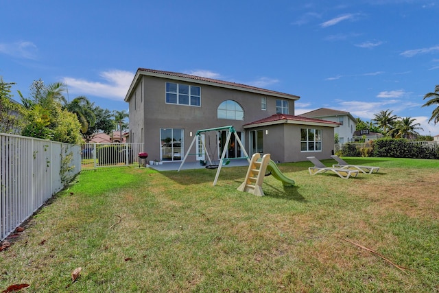 rear view of house with a lawn, a fenced backyard, a patio area, stucco siding, and a playground