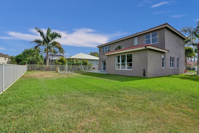 rear view of house with a lawn, stucco siding, a tile roof, and a fenced backyard