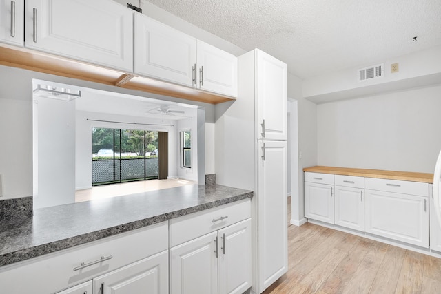 kitchen with white cabinets, a textured ceiling, visible vents, ceiling fan, and light wood-style floors