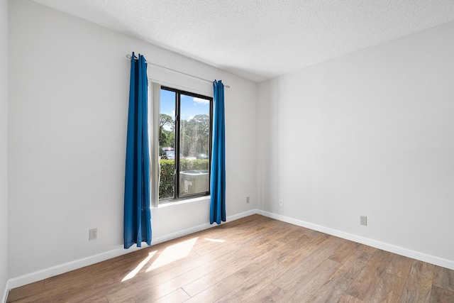 spare room featuring a textured ceiling, wood finished floors, and baseboards