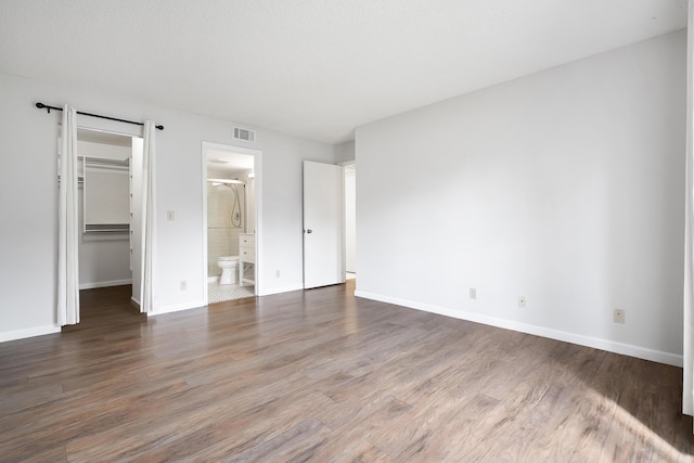 unfurnished bedroom featuring baseboards, a spacious closet, visible vents, and wood finished floors