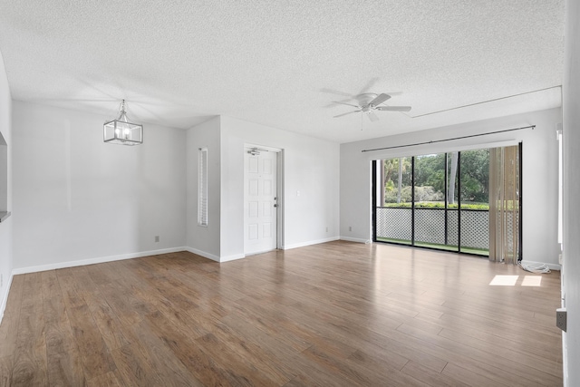 unfurnished living room featuring a textured ceiling, ceiling fan with notable chandelier, baseboards, and wood finished floors