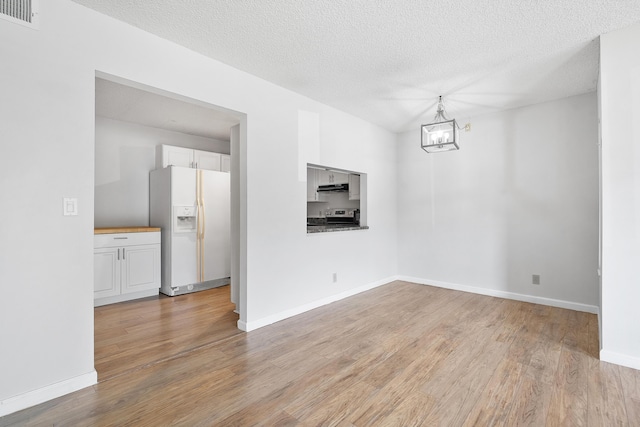 unfurnished dining area with a notable chandelier, a textured ceiling, light wood-type flooring, visible vents, and baseboards