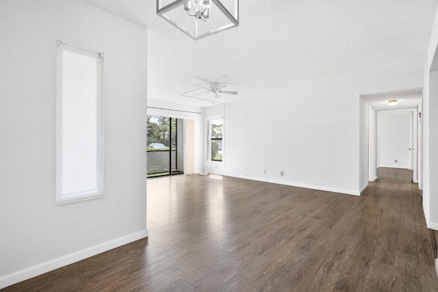 unfurnished living room featuring a textured ceiling, baseboards, a ceiling fan, and dark wood finished floors