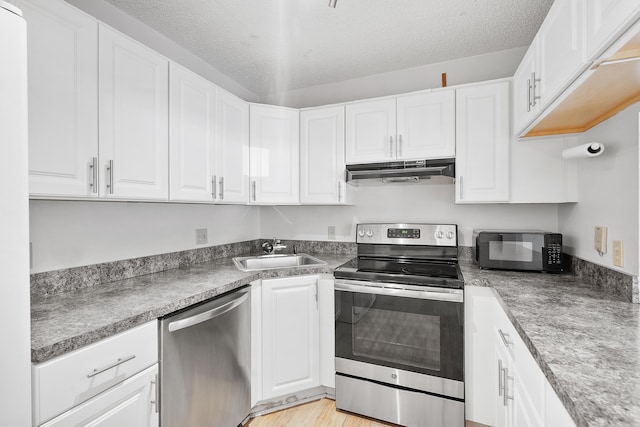 kitchen featuring a sink, stainless steel appliances, a textured ceiling, white cabinetry, and under cabinet range hood