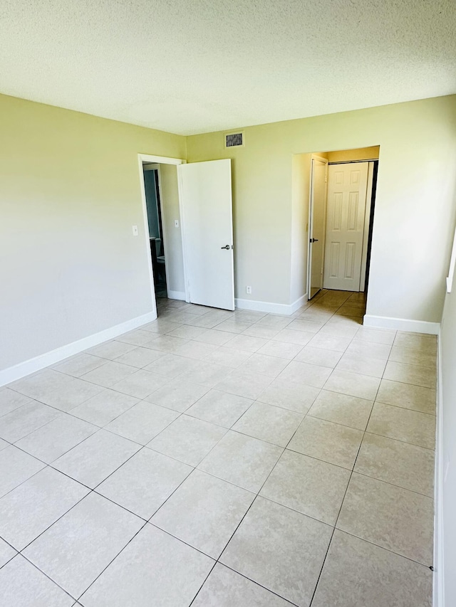 empty room with light tile patterned floors, visible vents, and baseboards