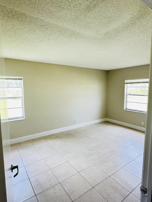 empty room with light tile patterned floors, baseboards, and a textured ceiling