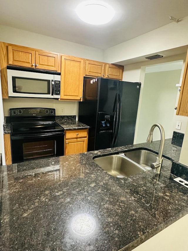 kitchen with black appliances, dark stone counters, visible vents, and a sink