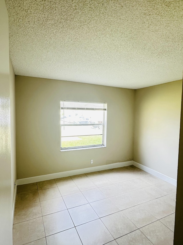 spare room featuring a textured ceiling, baseboards, and light tile patterned floors