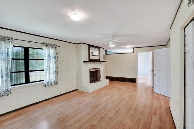 unfurnished living room with ceiling fan, light wood-style floors, wooden walls, baseboards, and a fireplace