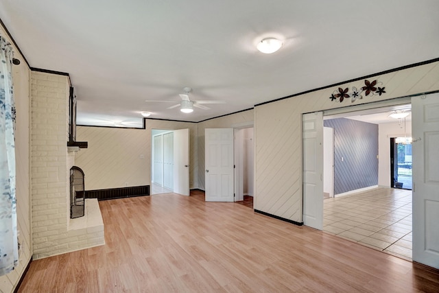 unfurnished living room with ceiling fan, light wood finished floors, baseboards, a fireplace, and wooden walls