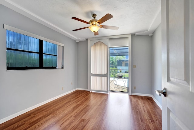 spare room featuring a textured ceiling, wood finished floors, baseboards, and ceiling fan