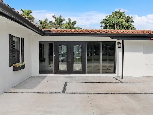view of exterior entry with a tiled roof, stucco siding, and french doors