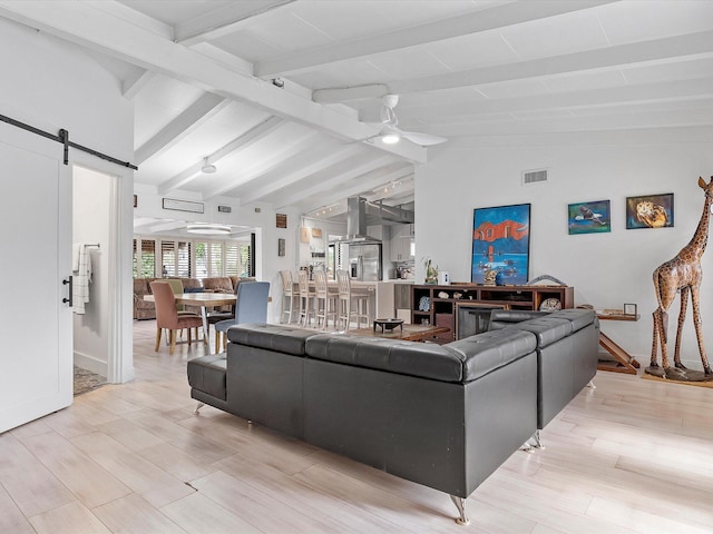 living room featuring light wood finished floors, a ceiling fan, vaulted ceiling with beams, visible vents, and a barn door