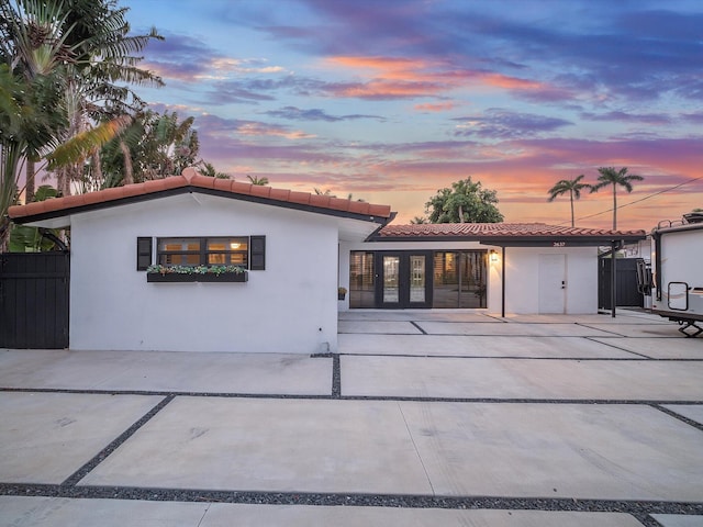 back of house at dusk with a tile roof, a patio, and stucco siding
