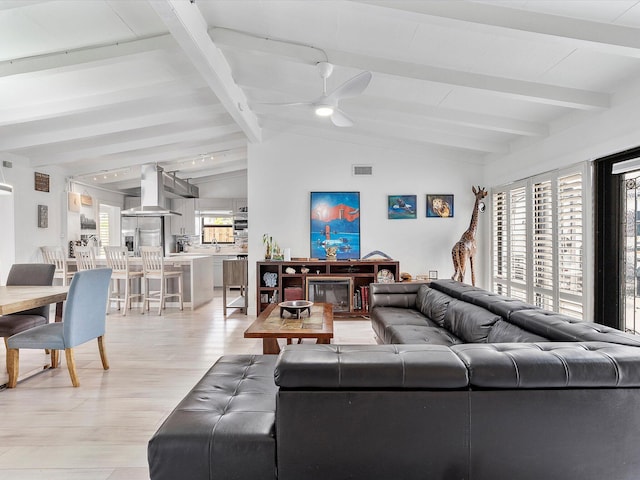 living area with visible vents, light wood-style flooring, ceiling fan, and vaulted ceiling with beams