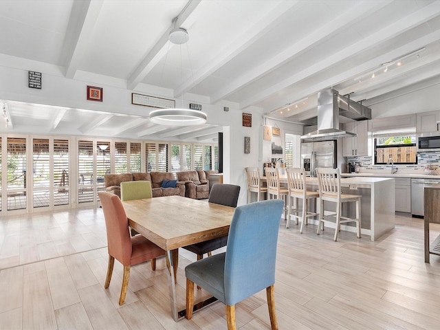 dining space with rail lighting, light wood-style flooring, and lofted ceiling with beams