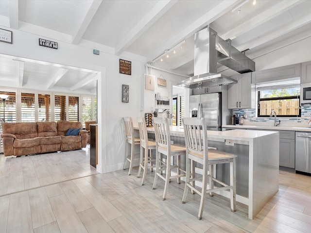 kitchen with wall chimney range hood, beam ceiling, rail lighting, light countertops, and gray cabinetry
