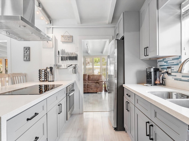 kitchen with a sink, wall chimney range hood, tasteful backsplash, beamed ceiling, and appliances with stainless steel finishes
