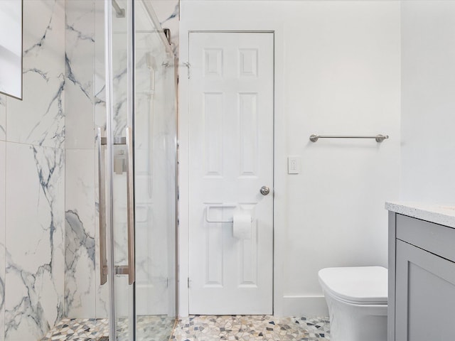 bathroom featuring vanity, toilet, a marble finish shower, and baseboards