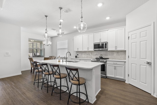 kitchen with stainless steel appliances, a sink, an island with sink, decorative backsplash, and light countertops