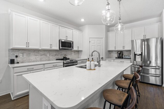 kitchen with stainless steel appliances, a sink, an island with sink, a kitchen bar, and white cabinetry