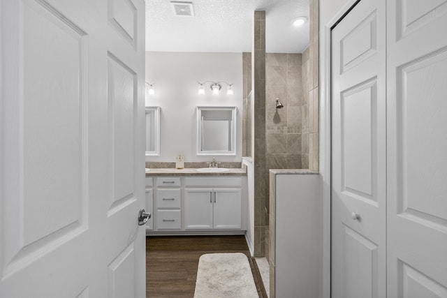 full bathroom featuring walk in shower, vanity, wood finished floors, and a textured ceiling