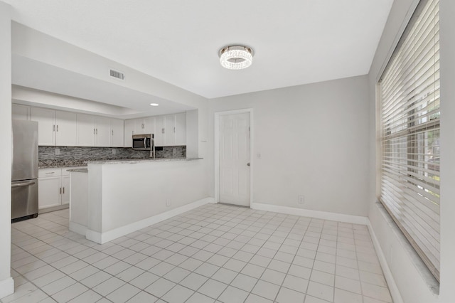 kitchen featuring stainless steel appliances, backsplash, white cabinetry, and light stone counters