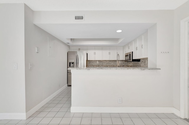 kitchen with stainless steel appliances, white cabinetry, a peninsula, a raised ceiling, and baseboards
