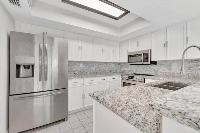 kitchen featuring appliances with stainless steel finishes, a sink, a raised ceiling, light tile patterned floors, and light stone countertops