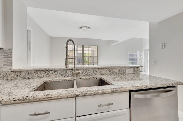 kitchen with stainless steel dishwasher, a sink, light stone counters, white cabinetry, and backsplash