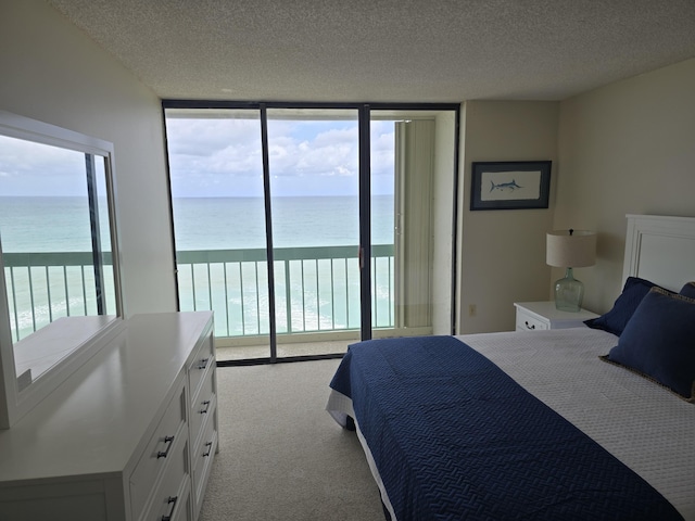 bedroom with a textured ceiling, carpet floors, a wall of windows, a water view, and access to exterior