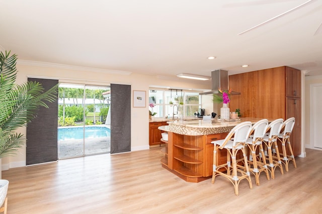 kitchen with brown cabinets, a kitchen bar, light wood-style flooring, open shelves, and exhaust hood