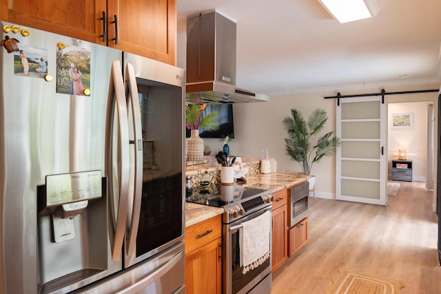 kitchen featuring brown cabinetry, appliances with stainless steel finishes, a barn door, range hood, and light wood-style floors