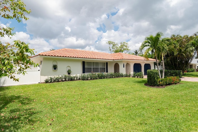 mediterranean / spanish home featuring fence, a tile roof, a garage, stucco siding, and a front lawn