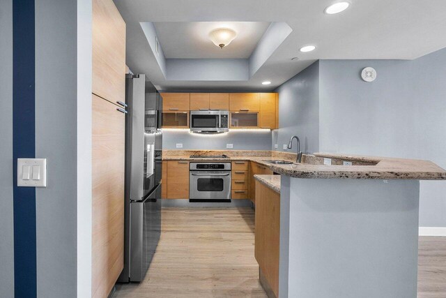 2640 Lake Shore Dr Unit 614, Riviera Beach, FL 33404 - kitchen with stainless steel appliances, a sink, a peninsula, light brown cabinetry, and light wood finished floors