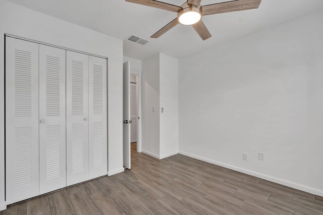 unfurnished bedroom featuring wood finished floors, a closet, baseboards, and a ceiling fan