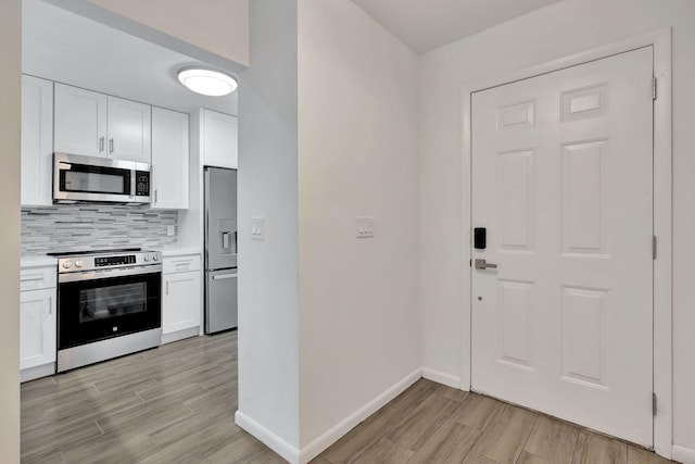 kitchen featuring appliances with stainless steel finishes, wood tiled floors, decorative backsplash, and white cabinetry
