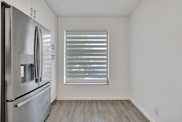kitchen featuring stainless steel refrigerator with ice dispenser, white cabinets, light wood-style flooring, and baseboards